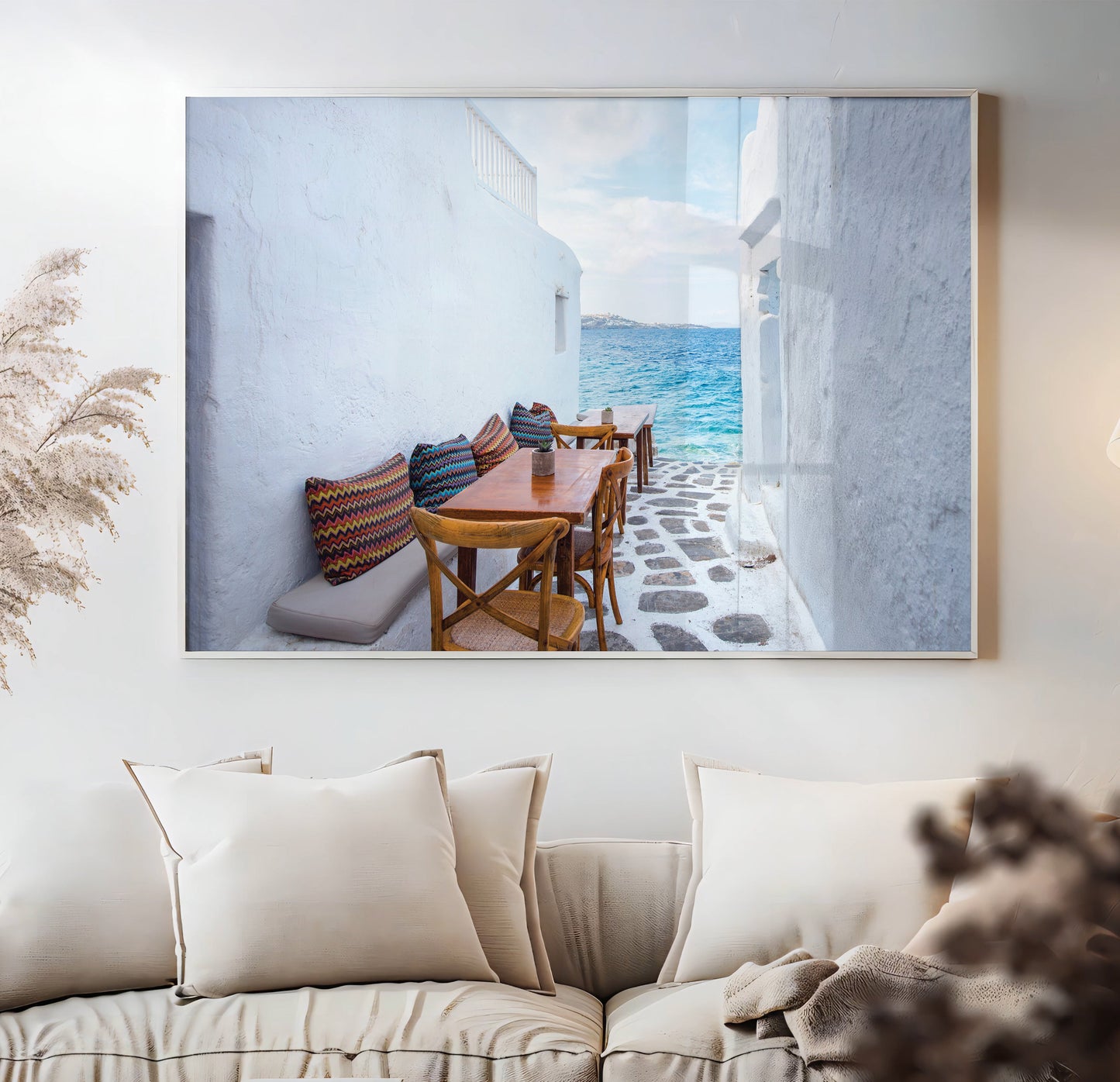 Framed artwork of a coastal scene with a table and chairs on a white wall above a beige sofa.