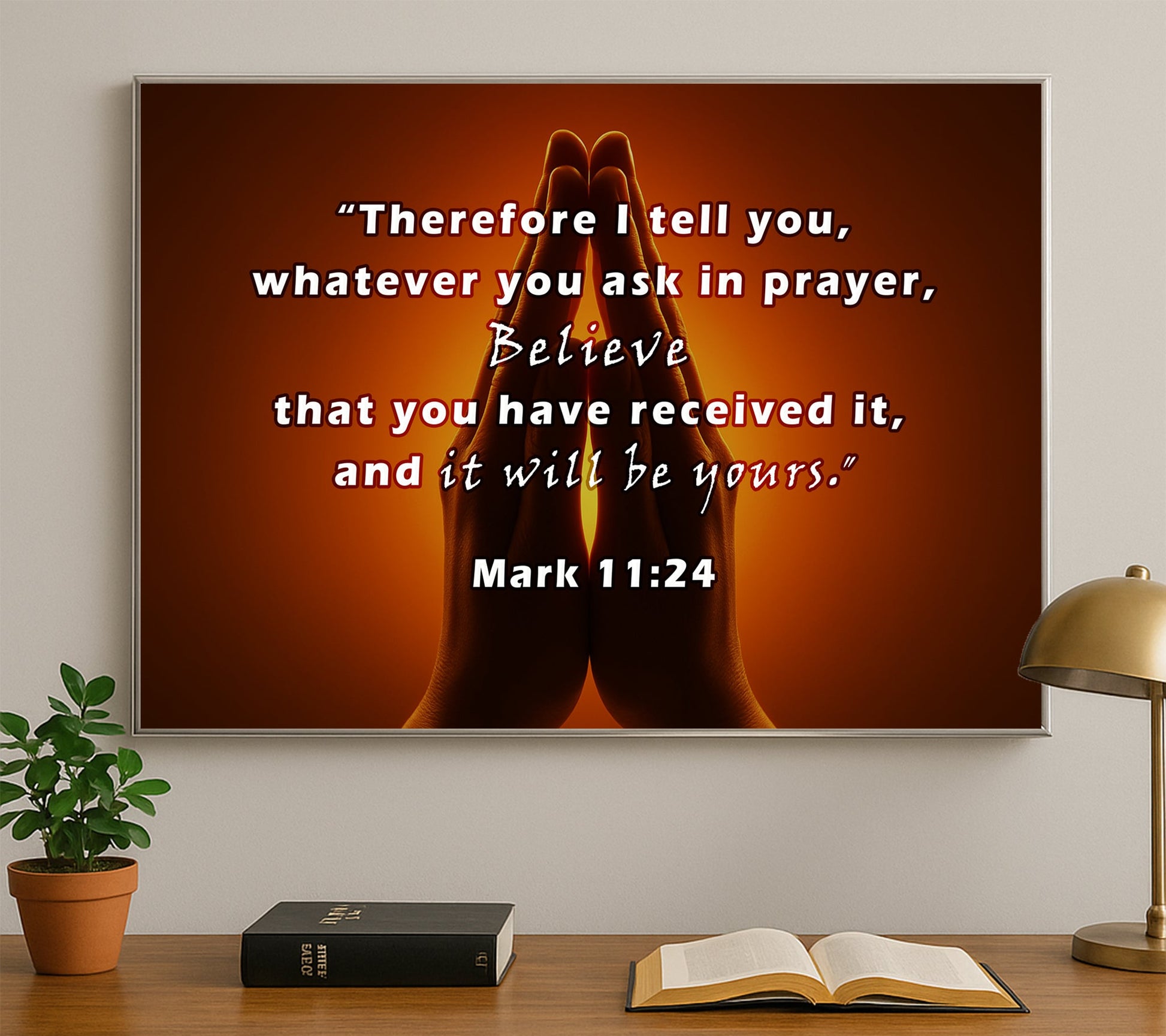 Praying hands with a quote on a wall above a desk with books and a lamp.